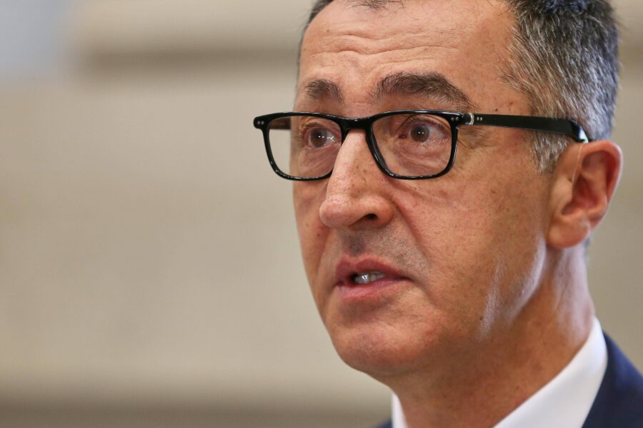 Mann mit Brille und Anzug spricht, Hintergrund unscharf.