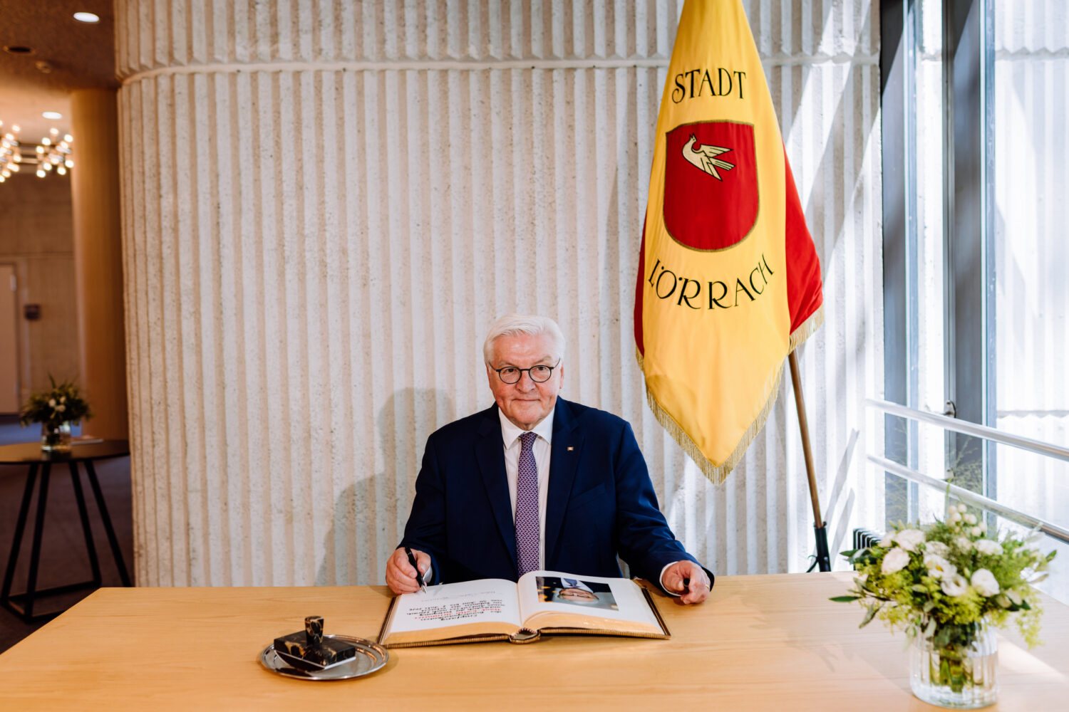 Älterer Mann am Tisch mit Buch, Flagge mit der Aufschrift "Stadt Lörrach".