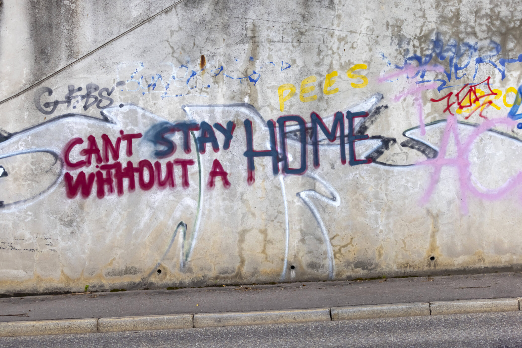 Graffiti an Wand, Text: "CAN'T STAY WITHOUT A HOME" in roten und blauen Buchstaben.