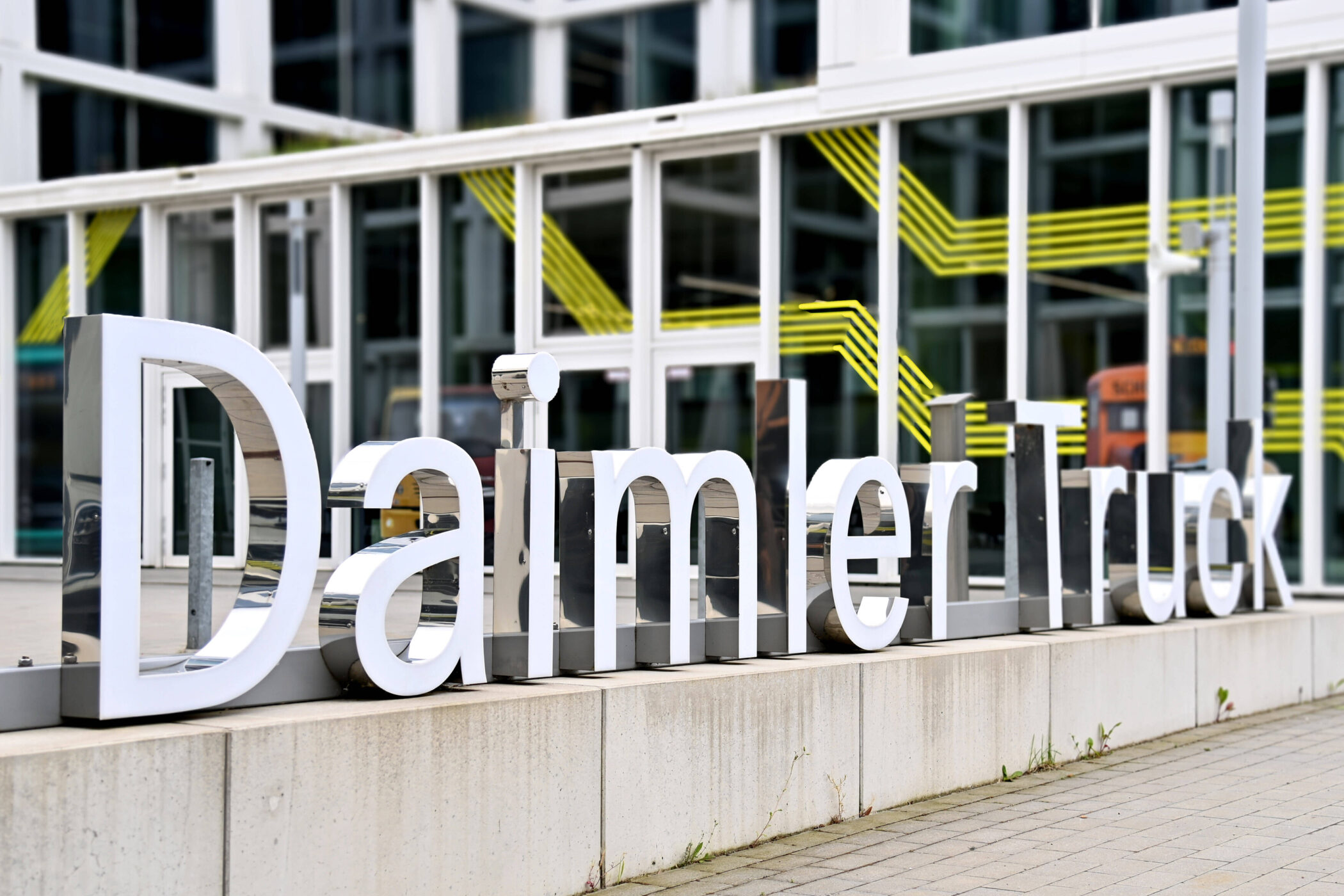 Schriftzug "Daimler Truck" vor einem Gebäude mit Glasfassade und gelben Linien.