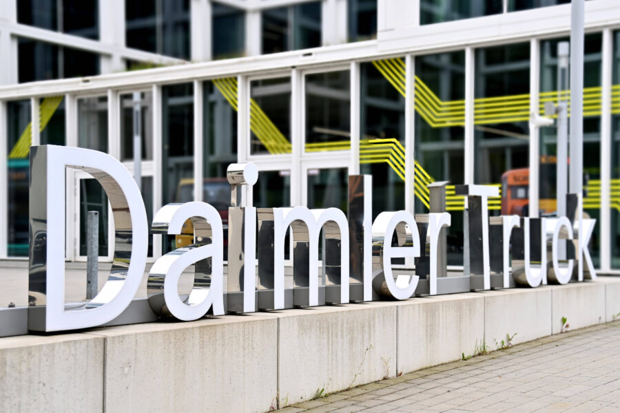 Schriftzug "Daimler Truck" vor einem Gebäude mit Glasfassade und gelben Linien.