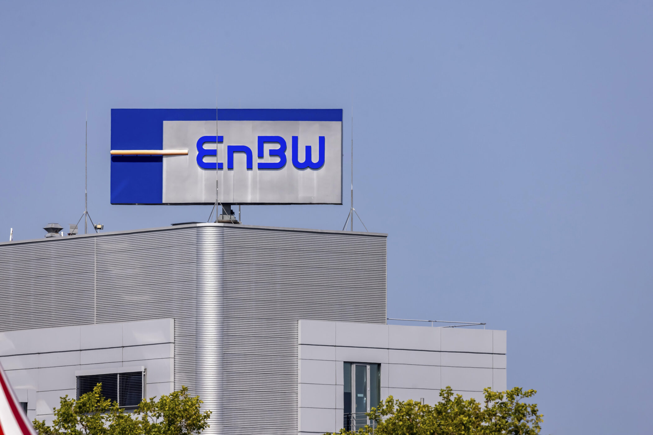 EnBW-Logo auf einem Gebäude mit grauen Fassadenpaneelen und blauer Himmel.