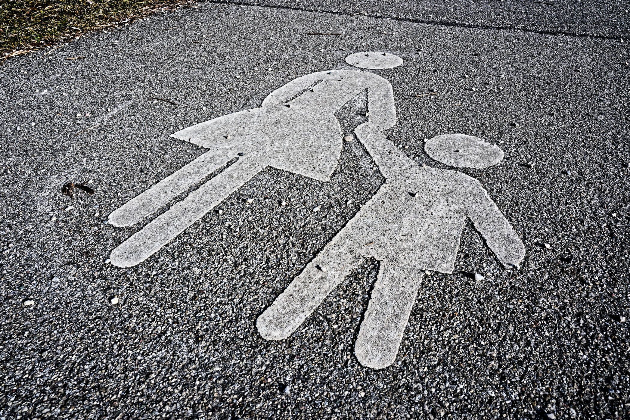 Zwei weiße Figuren auf Asphalt, Hand in Hand, eine mit Rock.