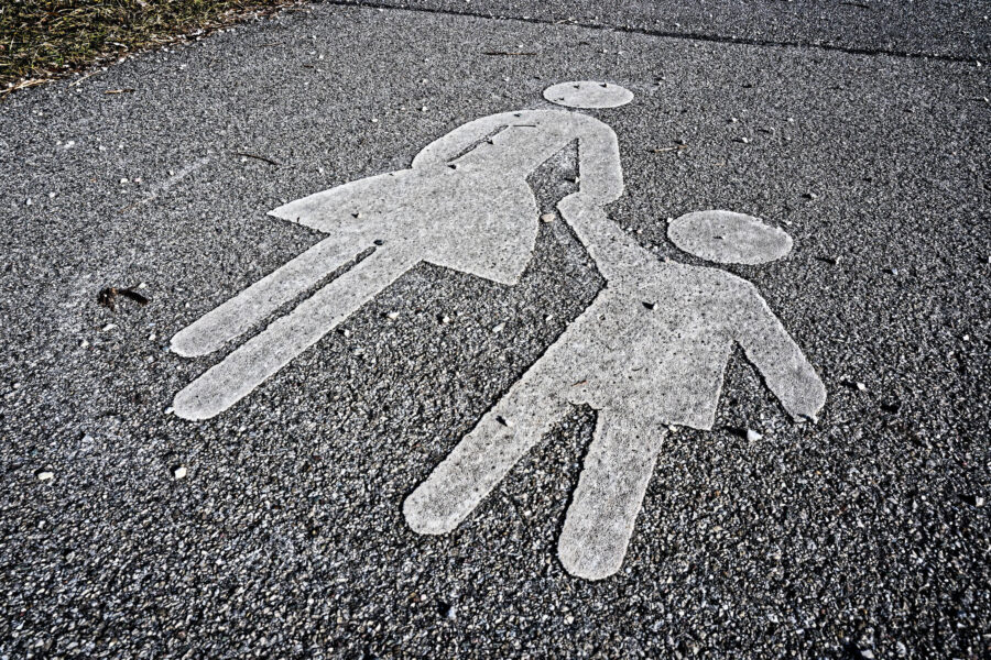 Zwei weiße Figuren auf Asphalt, Hand in Hand, eine mit Rock.
