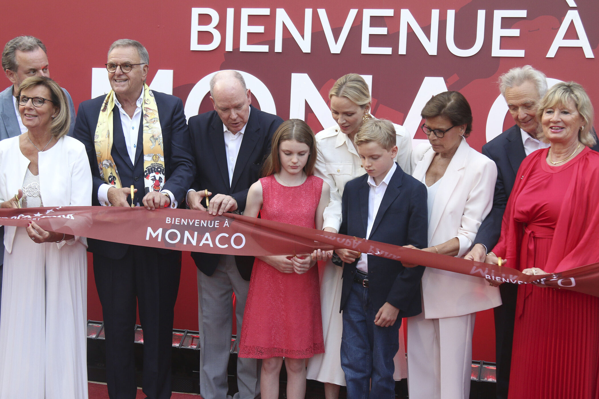 Neun Personen bei einer Zeremonie, halten ein Band mit „Bienvenue à Monaco“.