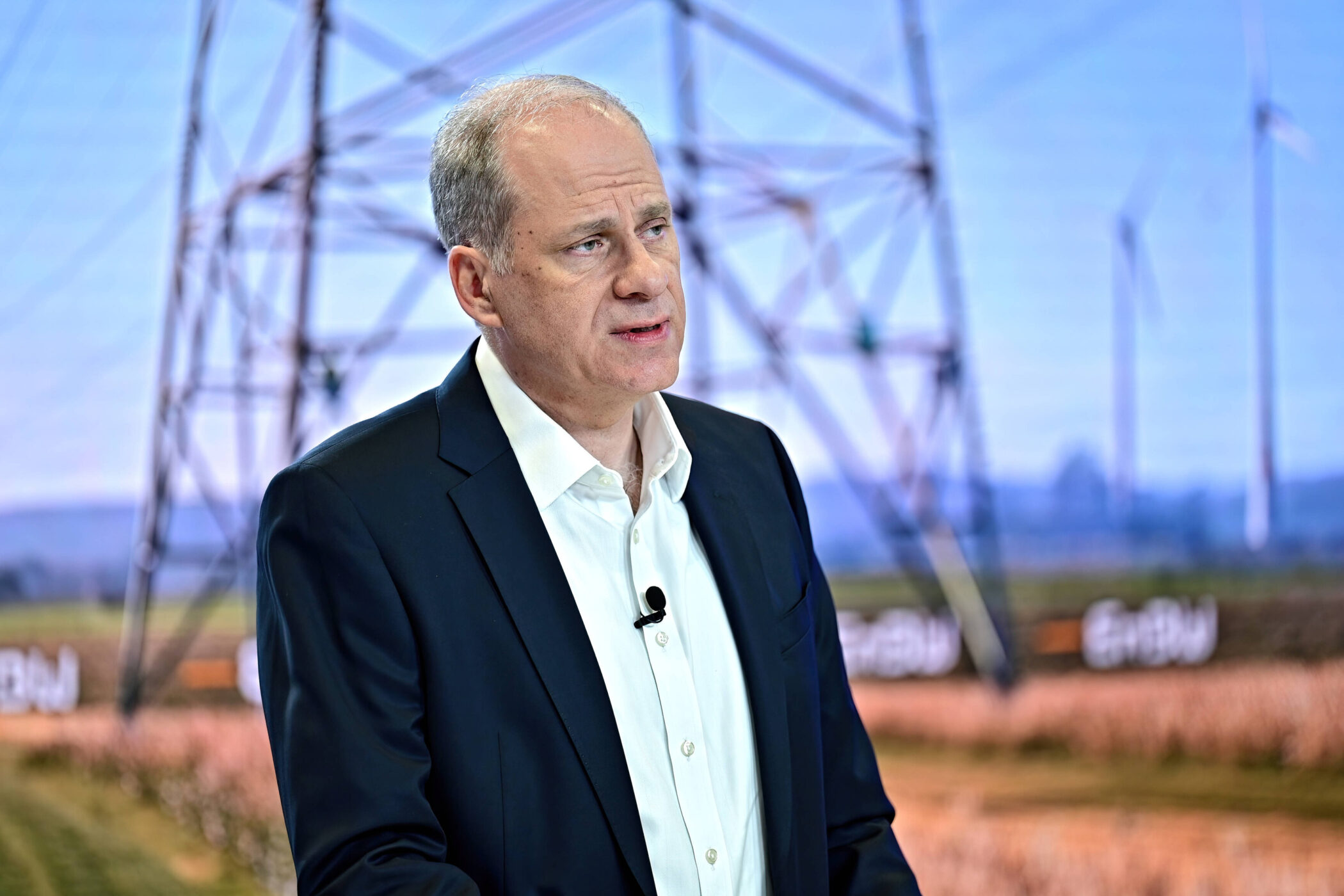 Eine Person mit Anzug im Freien, Strommast und Windkraftanlagen im Hintergrund.