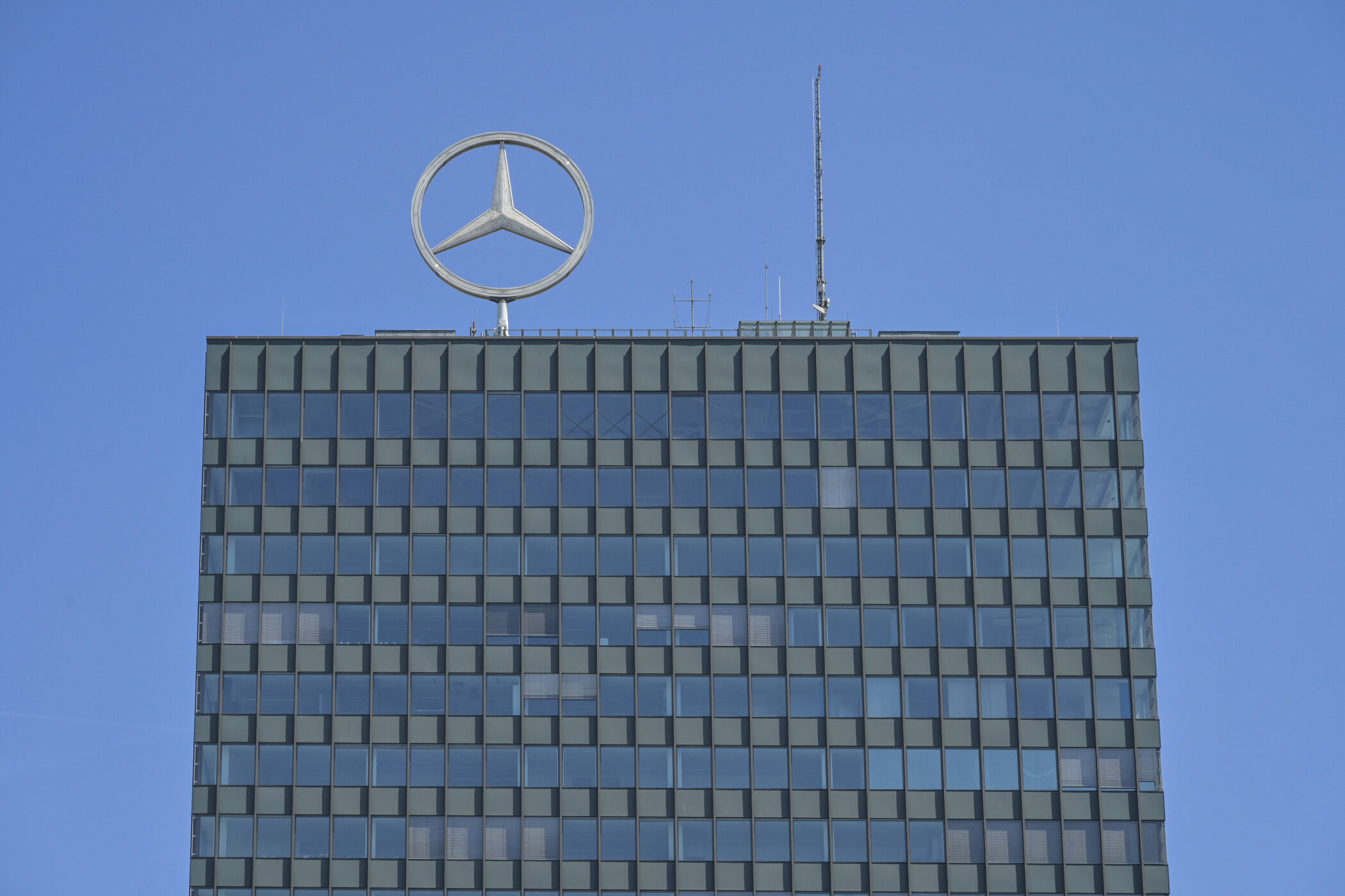 Hochhaus mit Mercedes-Stern auf dem Dach, blauer Himmel im Hintergrund.