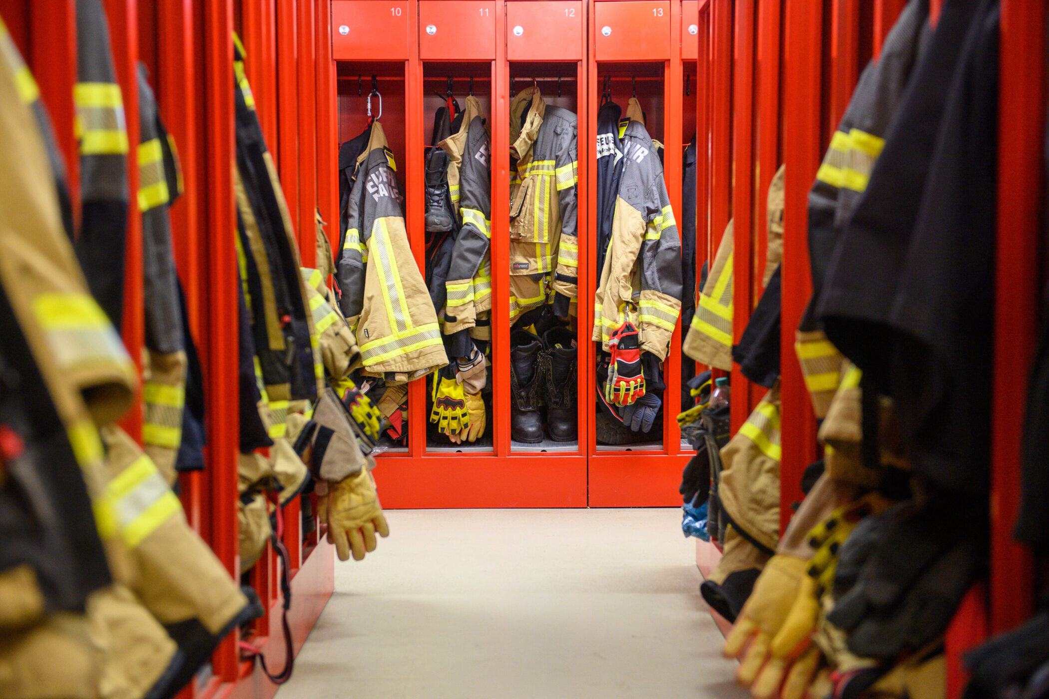 Rote Schränke mit Feuerwehranzügen, Helmen und Stiefeln in einem Umkleideraum.