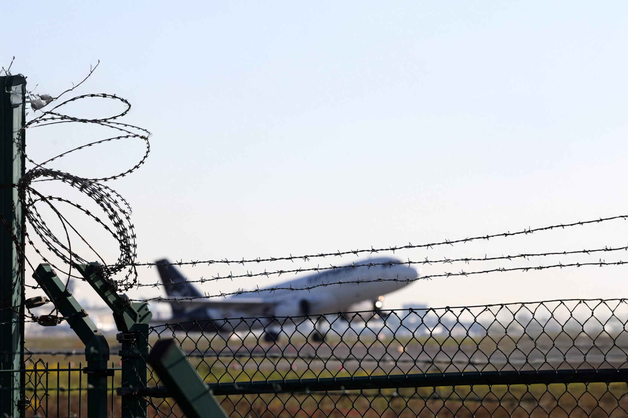 Flugzeug hinter Zaun mit Stacheldraht und klarem Himmel.