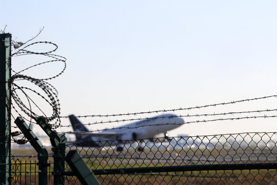Flugzeug hinter Zaun mit Stacheldraht und klarem Himmel.