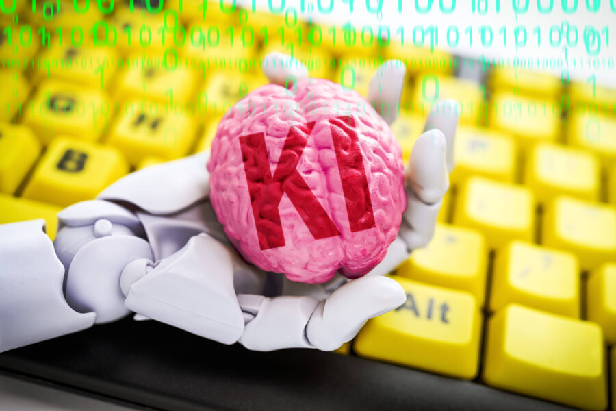 Roboterhand hält Gehirn mit Aufschrift "KI" über gelber Tastatur.