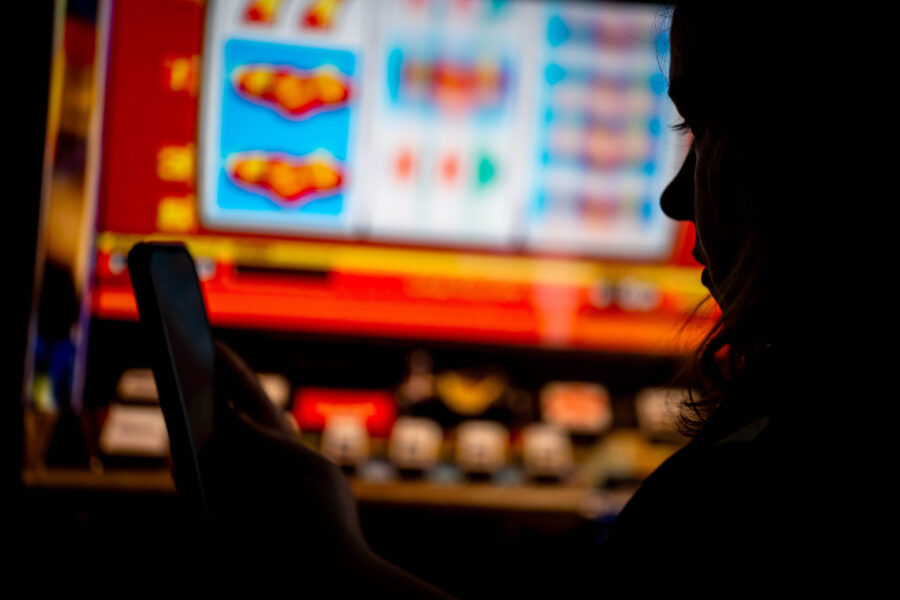 Person im Profil hält ein Smartphone, im Hintergrund bunte Slots-Anzeige.