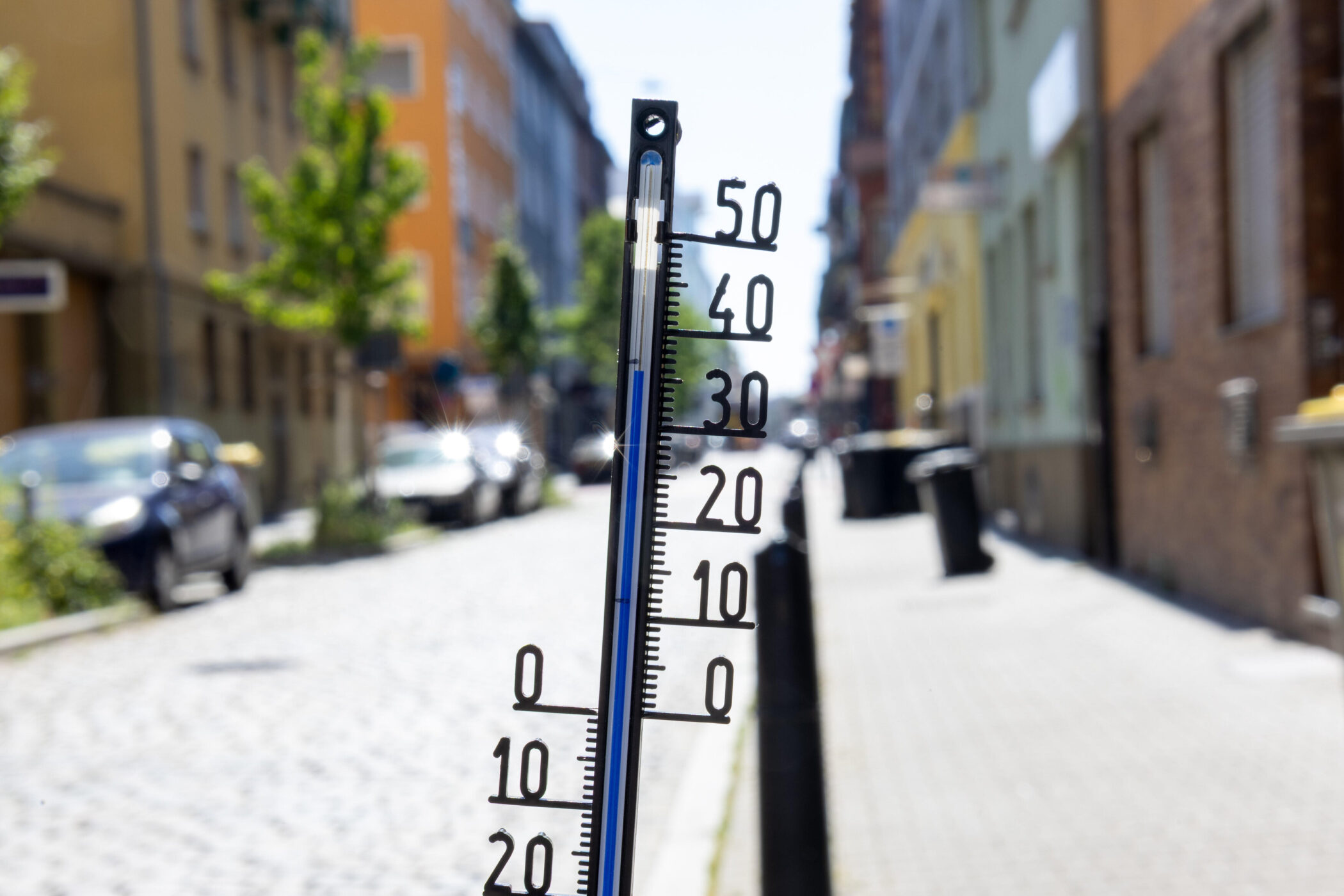 Thermometer zeigt 30 Grad, verschwommene Straße im Hintergrund.