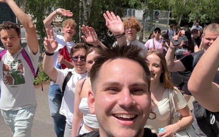 Gruppe von Menschen im Freien, viele winken und lächeln in die Kamera.