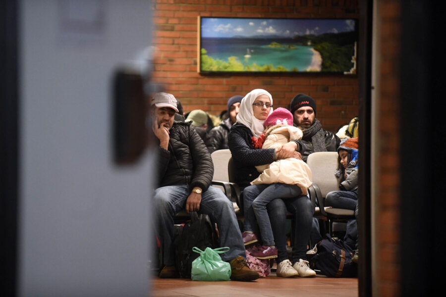 Mehrere Menschen sitzen auf Stühlen in einem Raum mit Backsteinwand.
