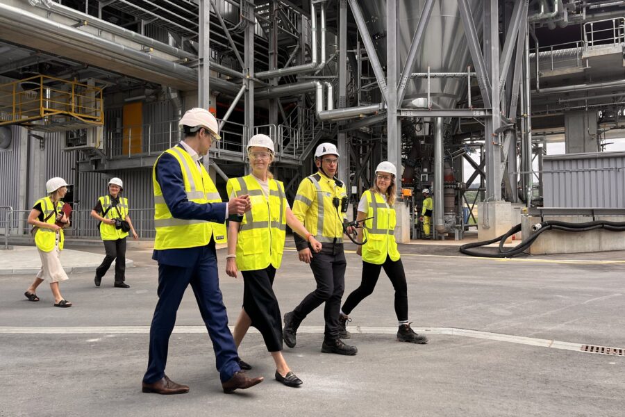 Sechs Personen in Sicherheitskleidung gehen in einer Industrieanlage.