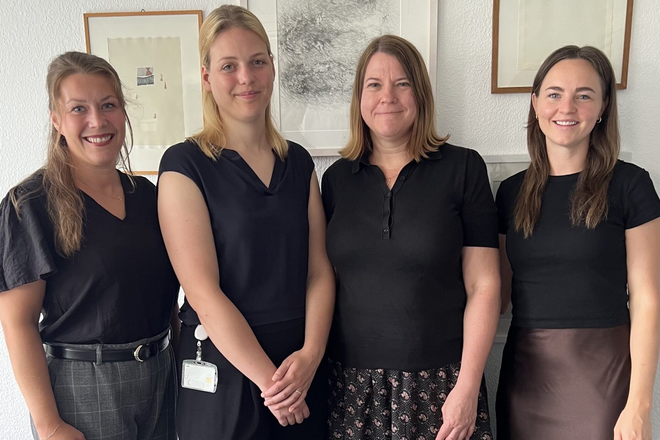 Vier Frauen stehen nebeneinander vor einer Wand mit drei Bildern.