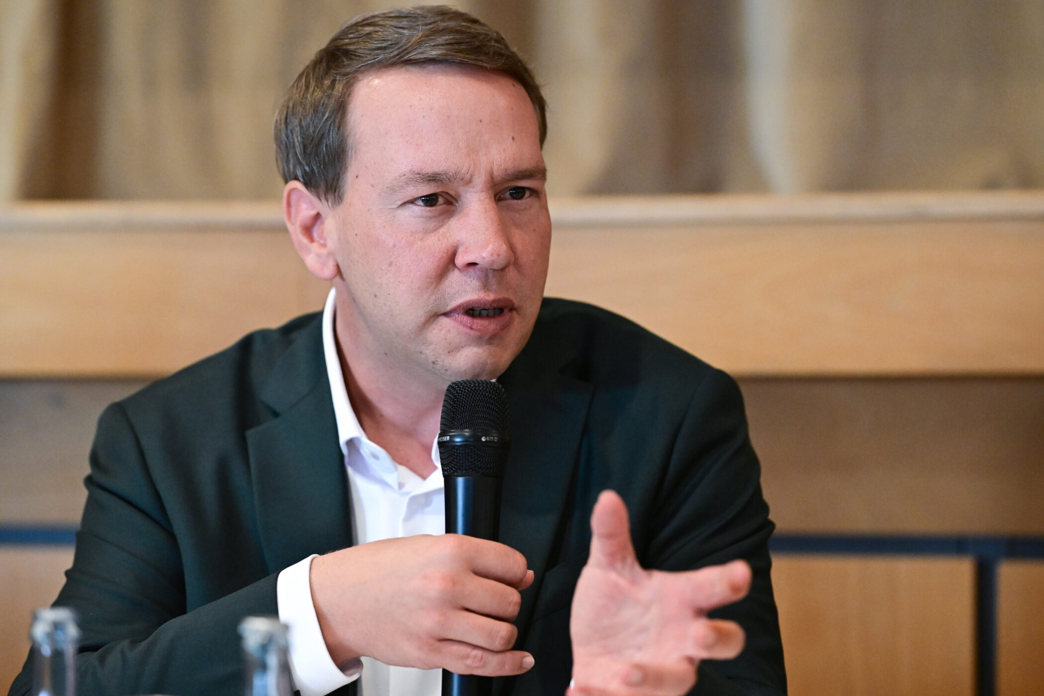 Person mit Mikrofon spricht, Hintergrund Holzvertäfelung.