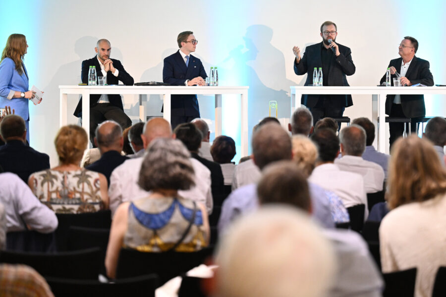 Fünf Personen auf der Bühne, Publikum im Vordergrund, blauer Hintergrund.
