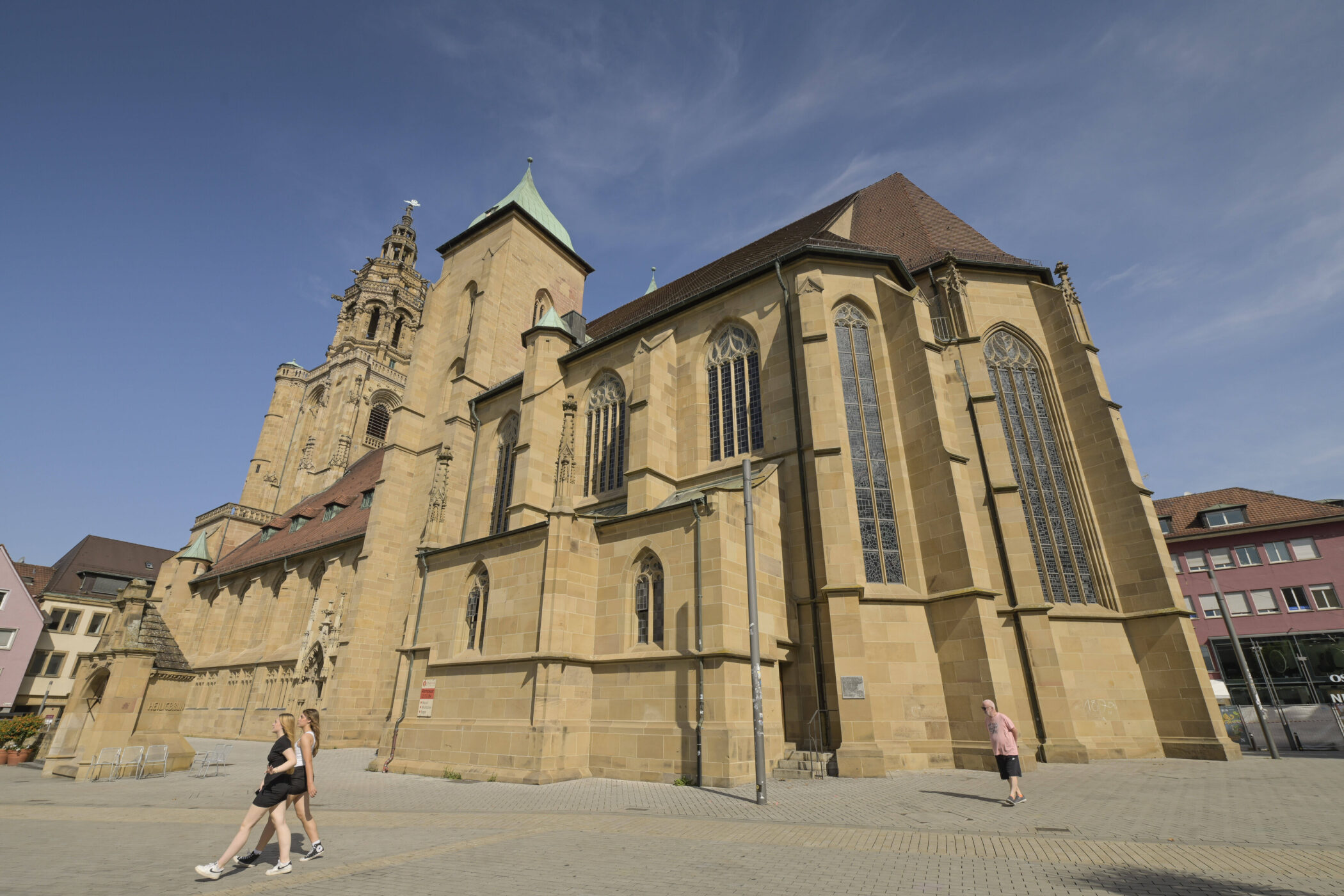Zwei Personen gehen vor einer großen gotischen Kirche mit hohen Fenstern vorbei.