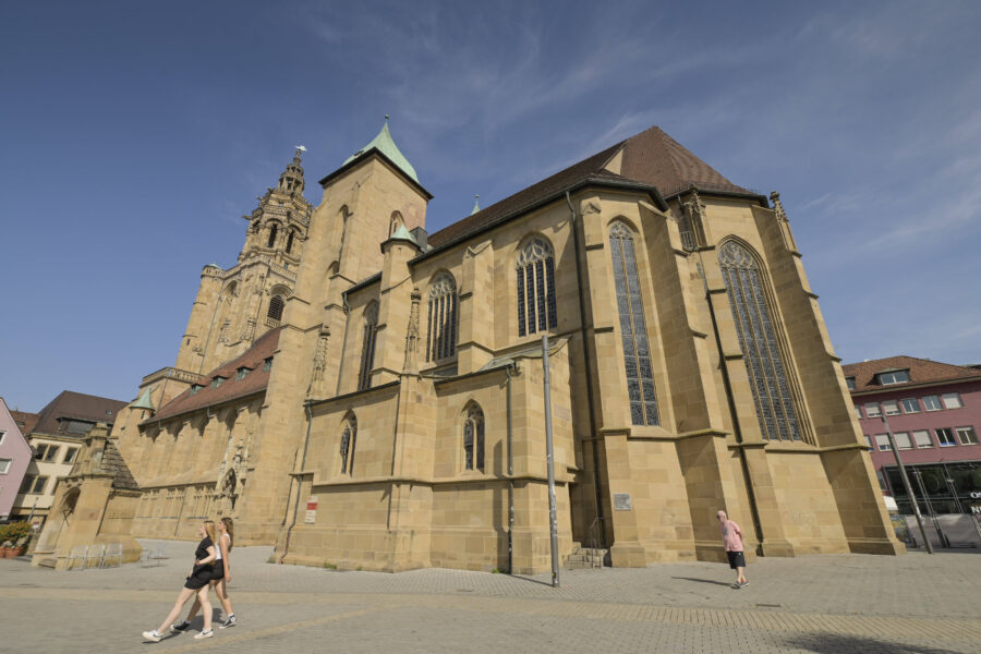 Zwei Personen gehen vor einer großen gotischen Kirche mit hohen Fenstern vorbei.