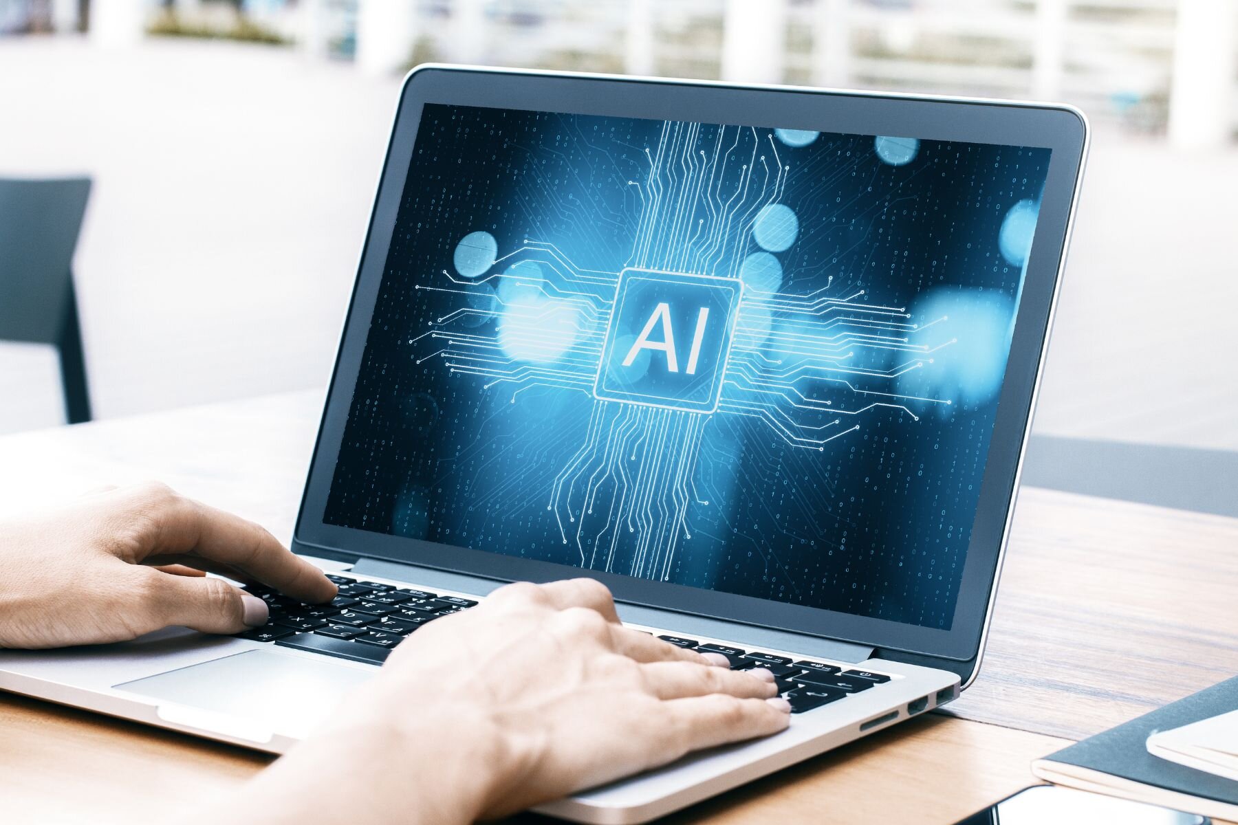 Laptop mit leuchtendem "AI"-Logo auf dem Bildschirm, Hände tippen auf Tastatur.