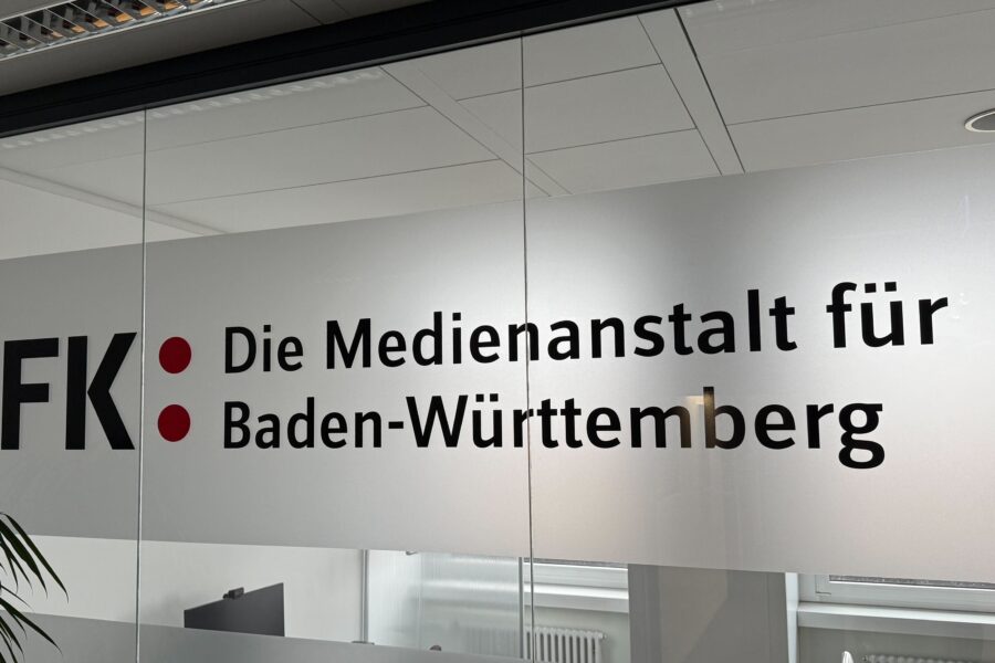 Glastür mit dem Text: LFK Die Medienanstalt für Baden-Württemberg. Pflanze links.