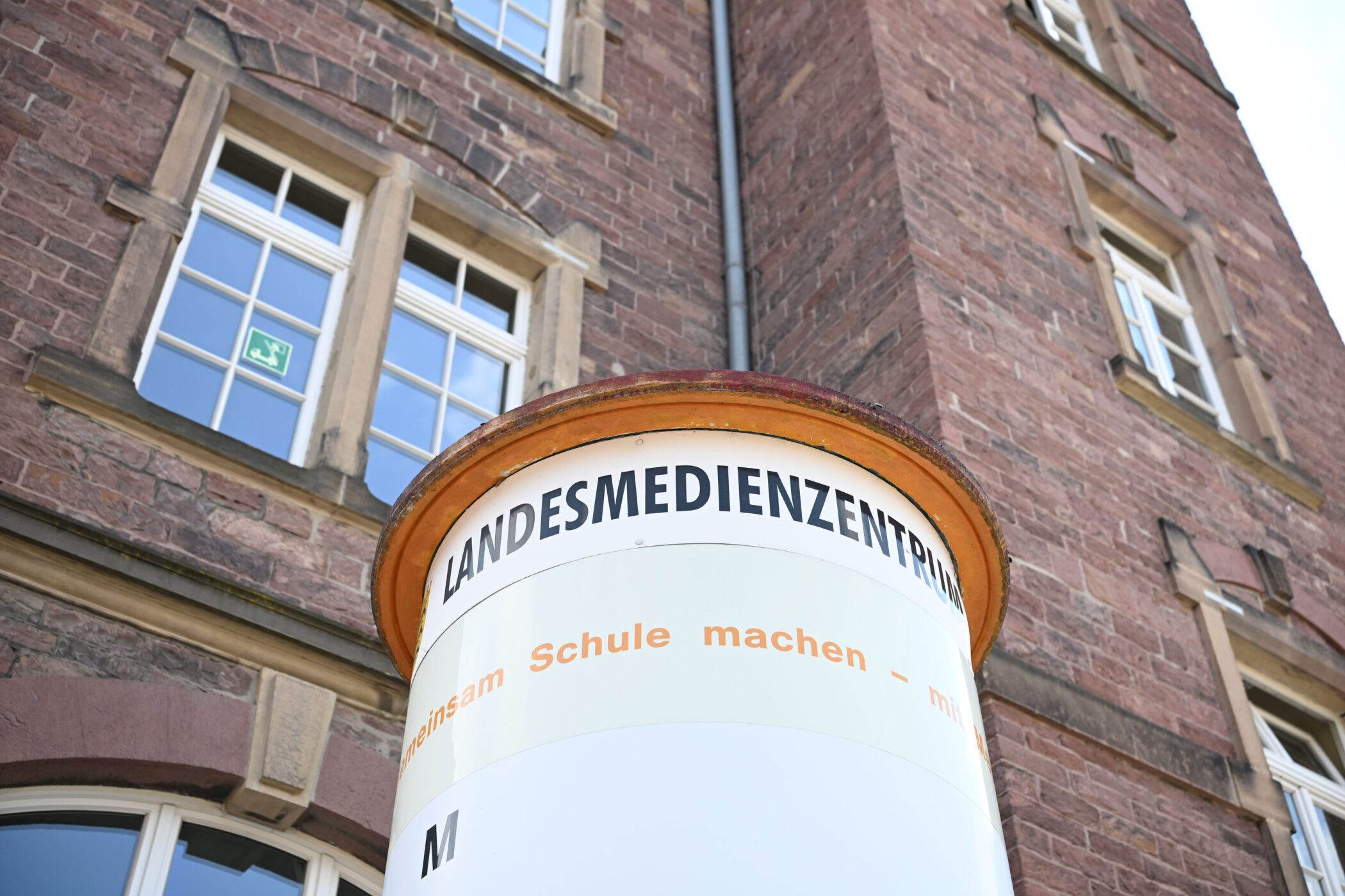 Ziegelgebäude mit Schild "LANDESMEDIENZENTRUM", zwei Fenster, Notausgangsschild.