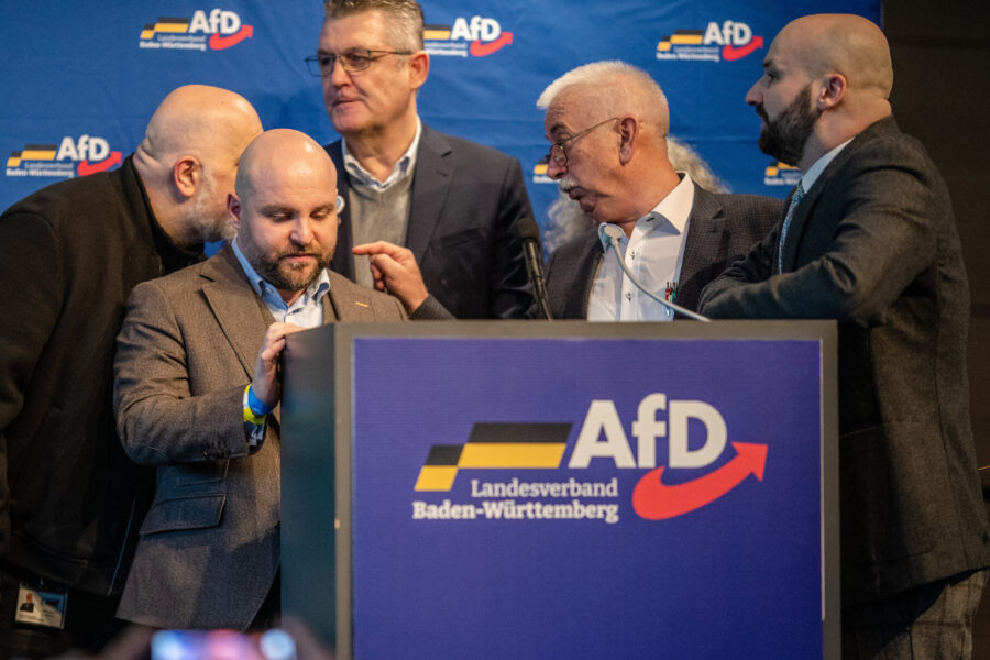 Fünf Männer an einem Rednerpult mit AfD-Logo und -Banner im Hintergrund.