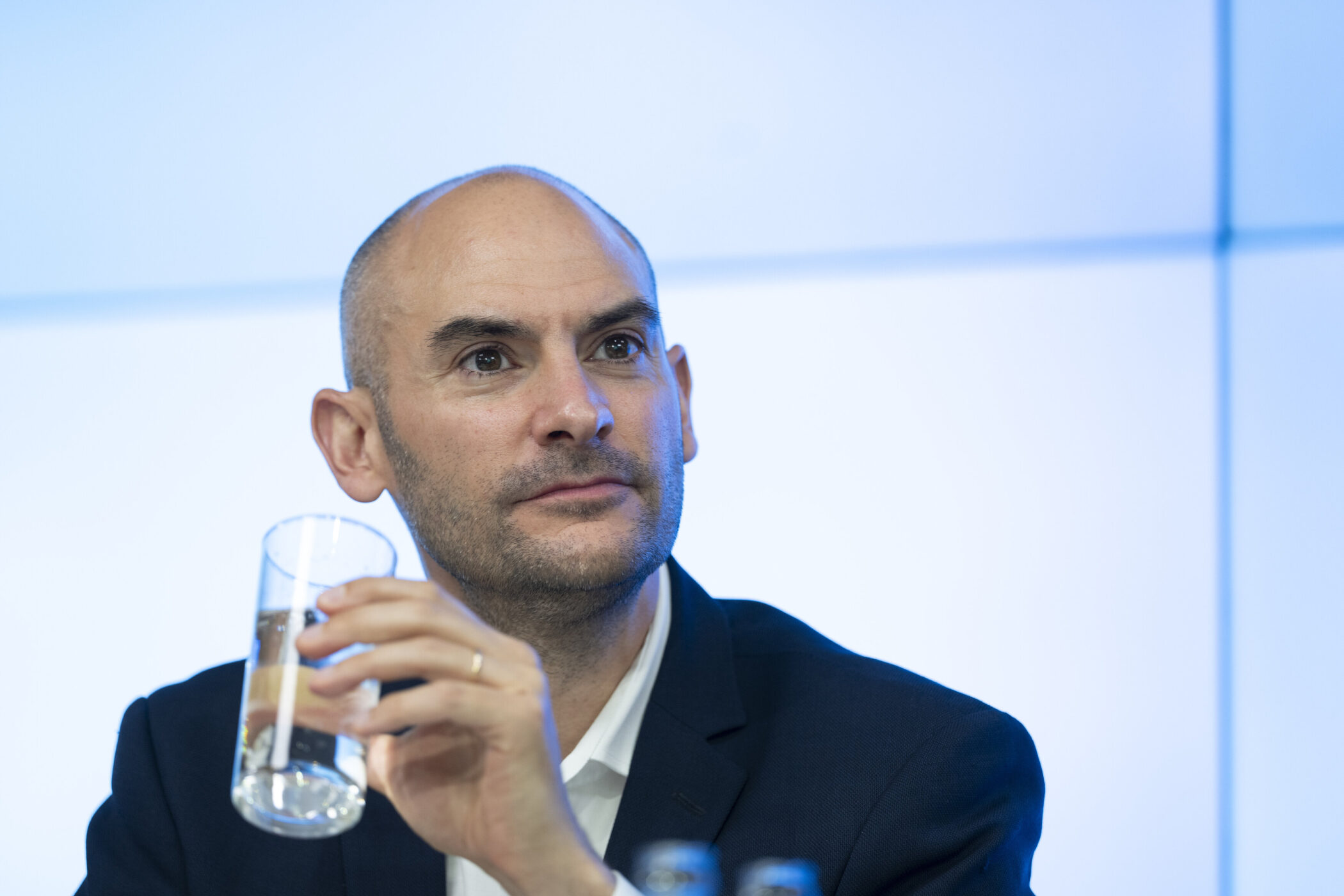 Mann im Anzug hält ein Glas Wasser. Hintergrund in Blau.