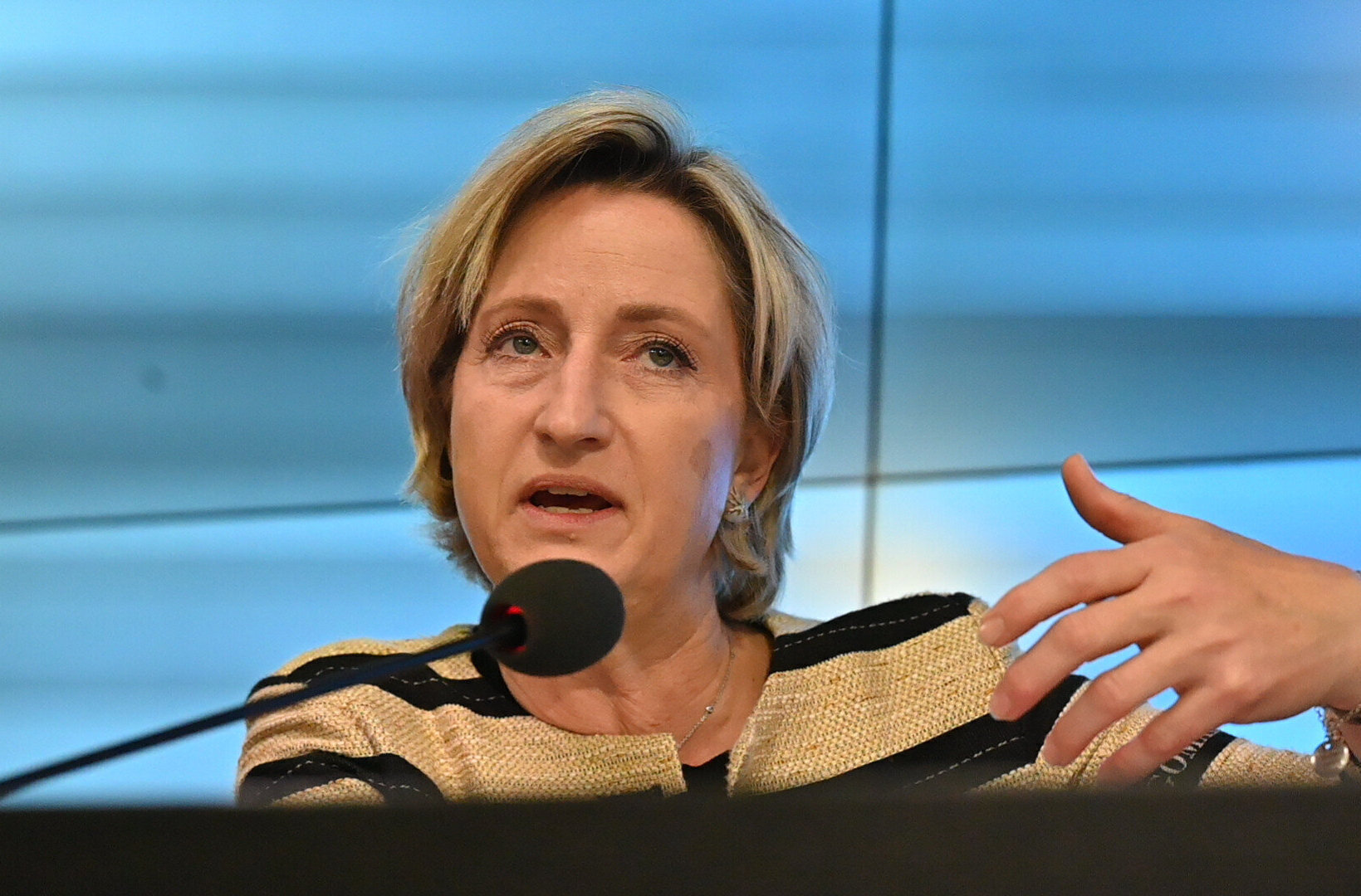 Frau spricht in ein Mikrofon, blaue Hintergrundwand.