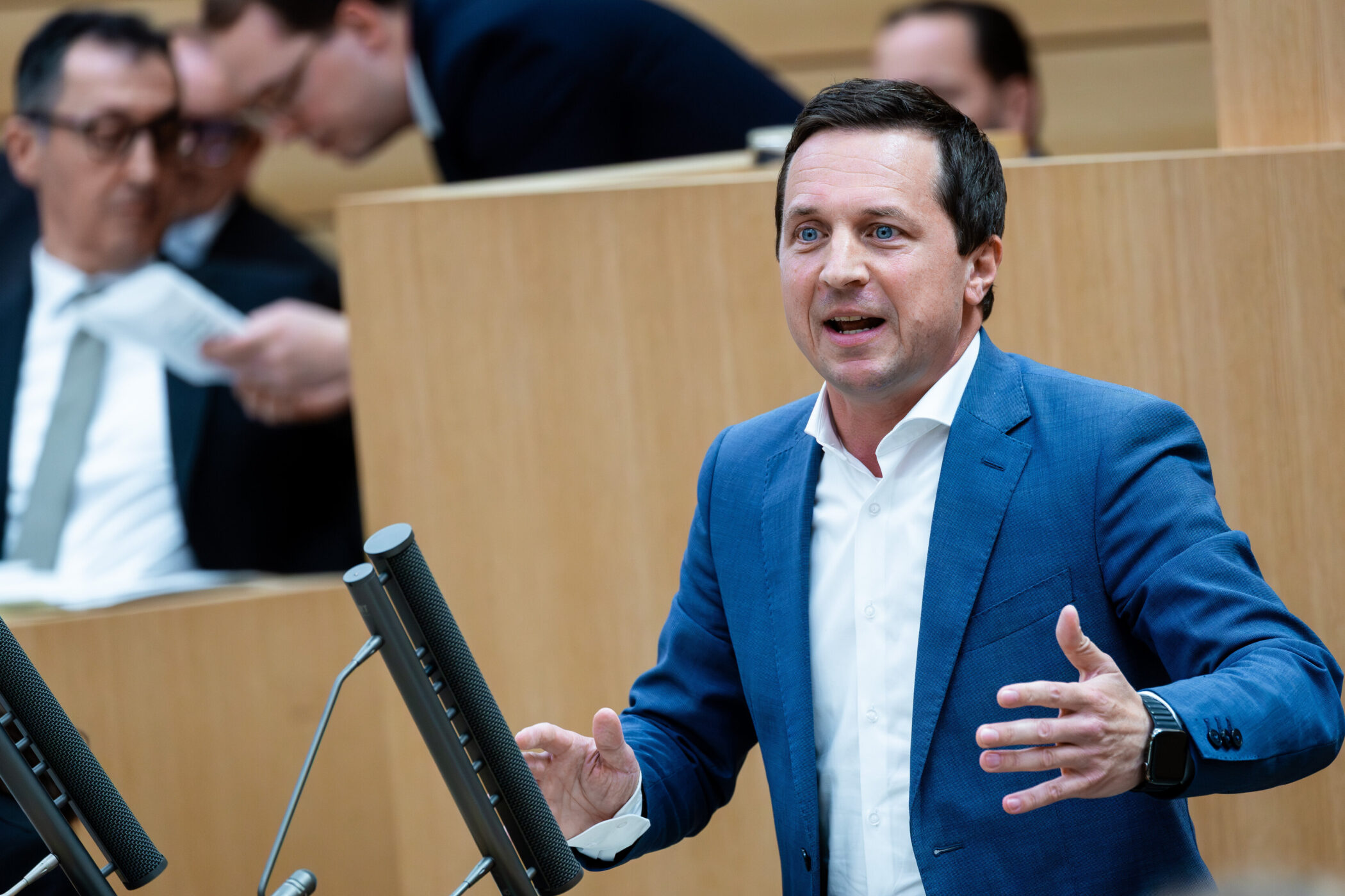 Ein Mann in blauem Anzug spricht vor zwei Mikrofonen.