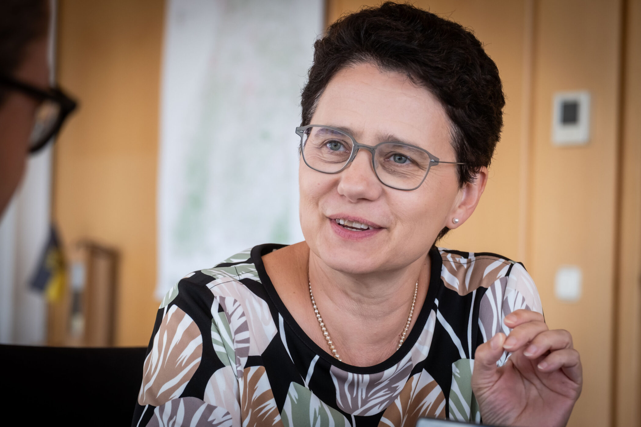 Zwei Menschen im Gespräch, eine Person mit Brille und gemustertem Oberteil.