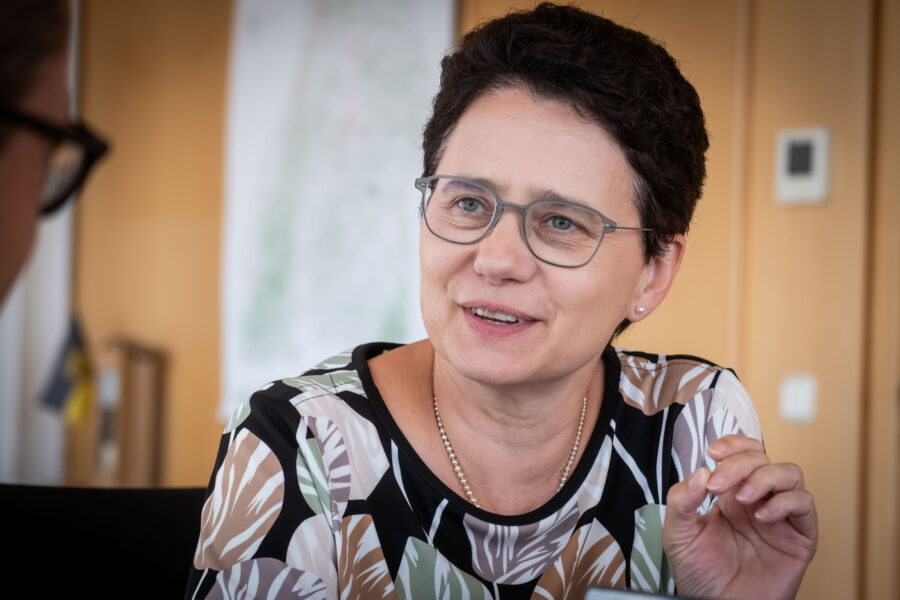 Zwei Menschen im Gespräch, eine Person mit Brille und gemustertem Oberteil.