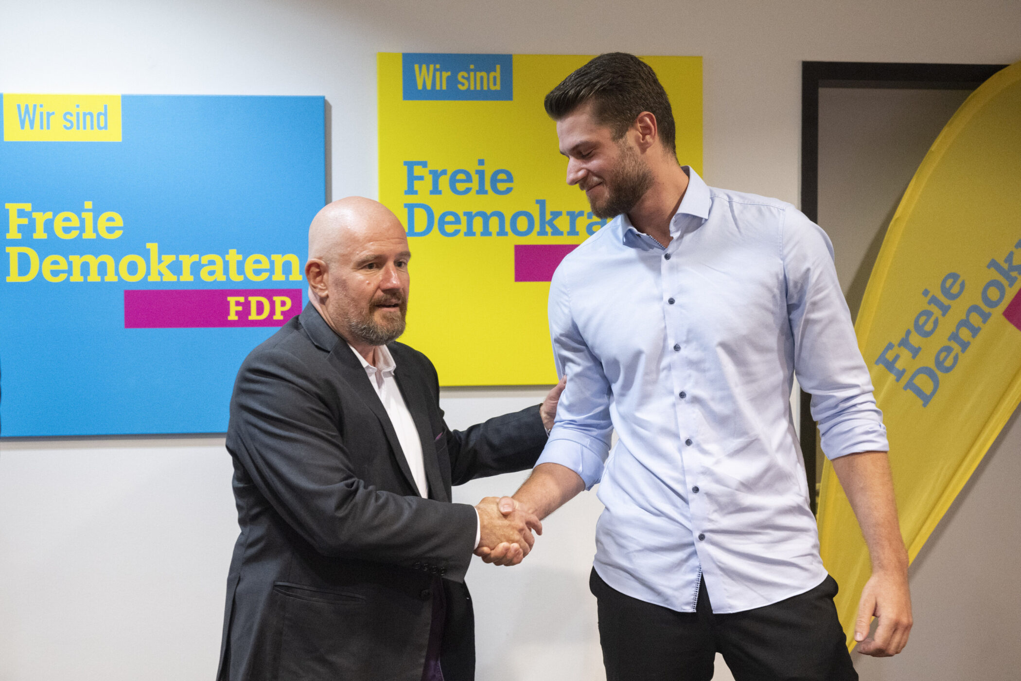 Zwei Männer schütteln Hände; FDP-Logos im Hintergrund.