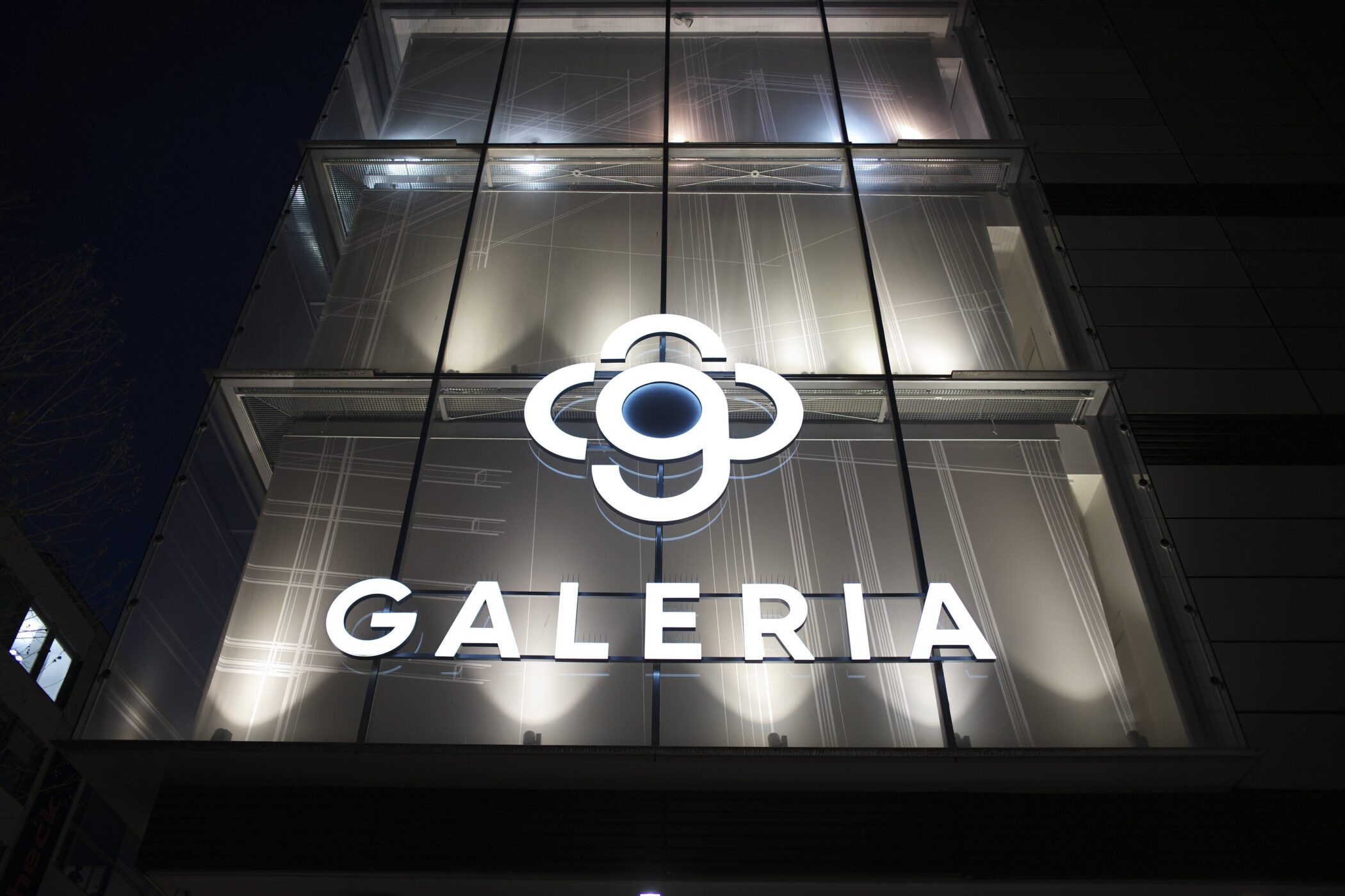 Galeria-Logo an einem Gebäude bei Nacht.