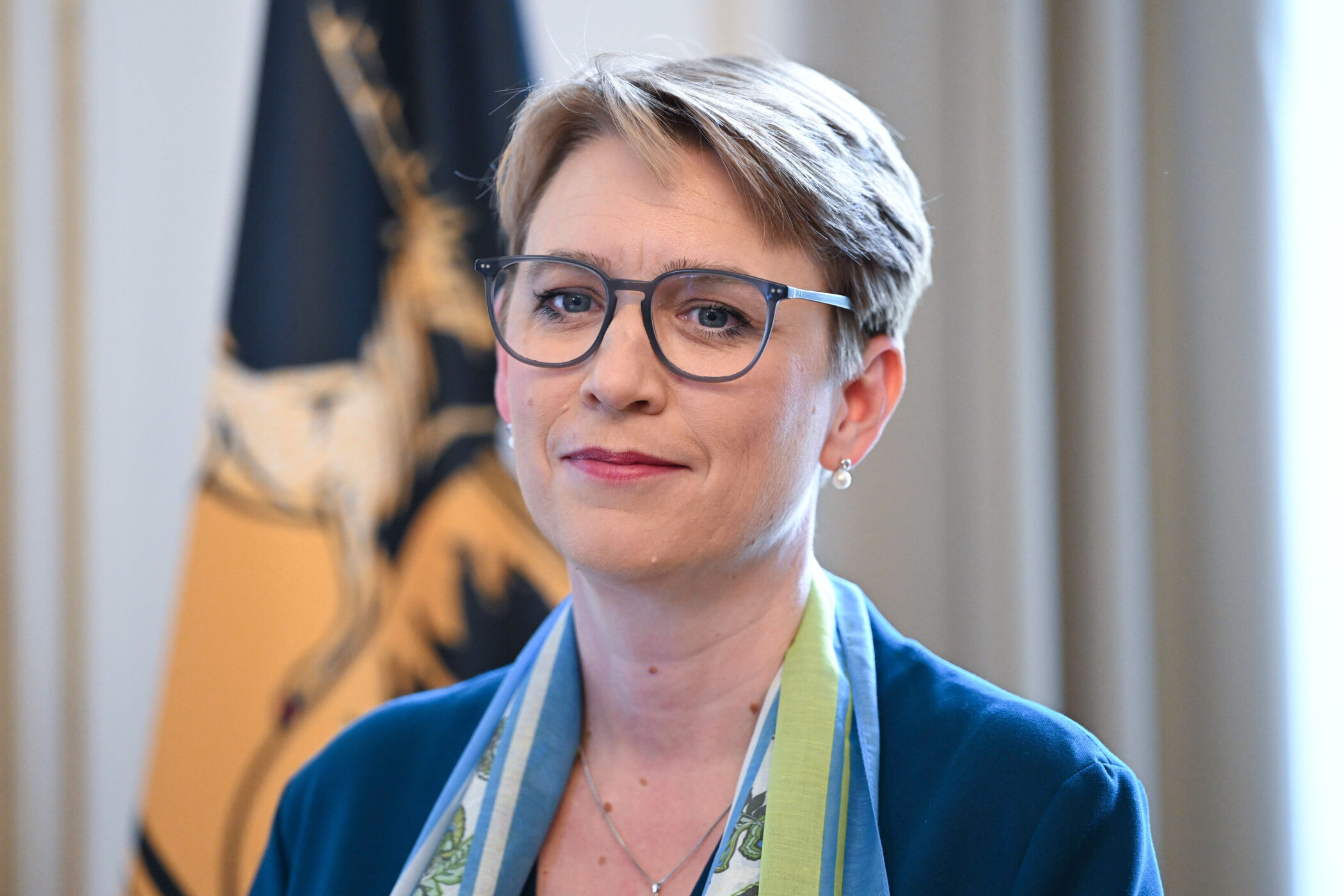 Eine Frau mit Brille und Schal vor einer Fahne.