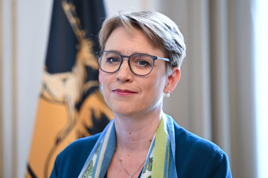 Eine Frau mit Brille und Schal vor einer Fahne.