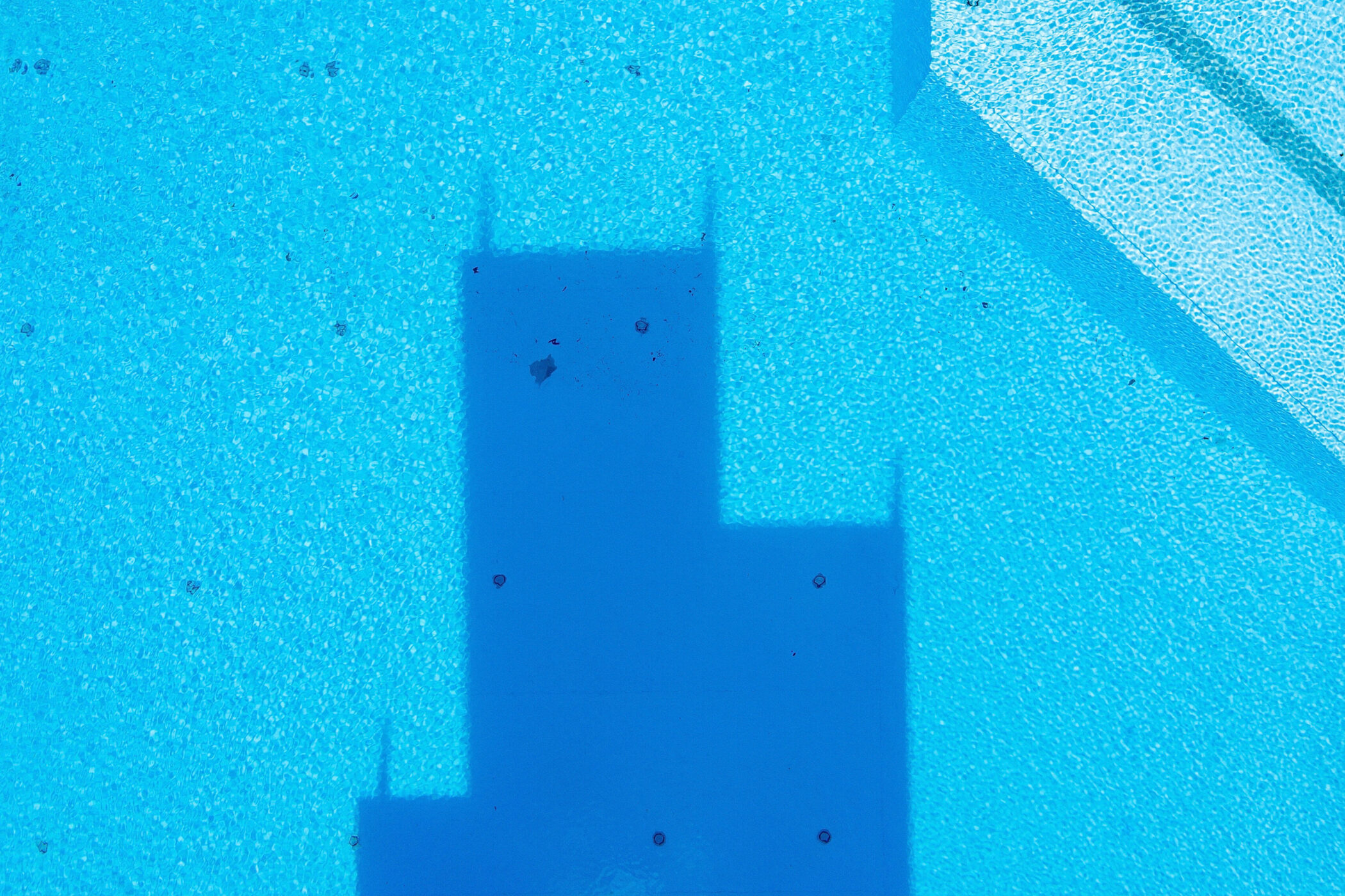 Blaue Wasseroberfläche mit mehreren dunklen Formen und Schatten.