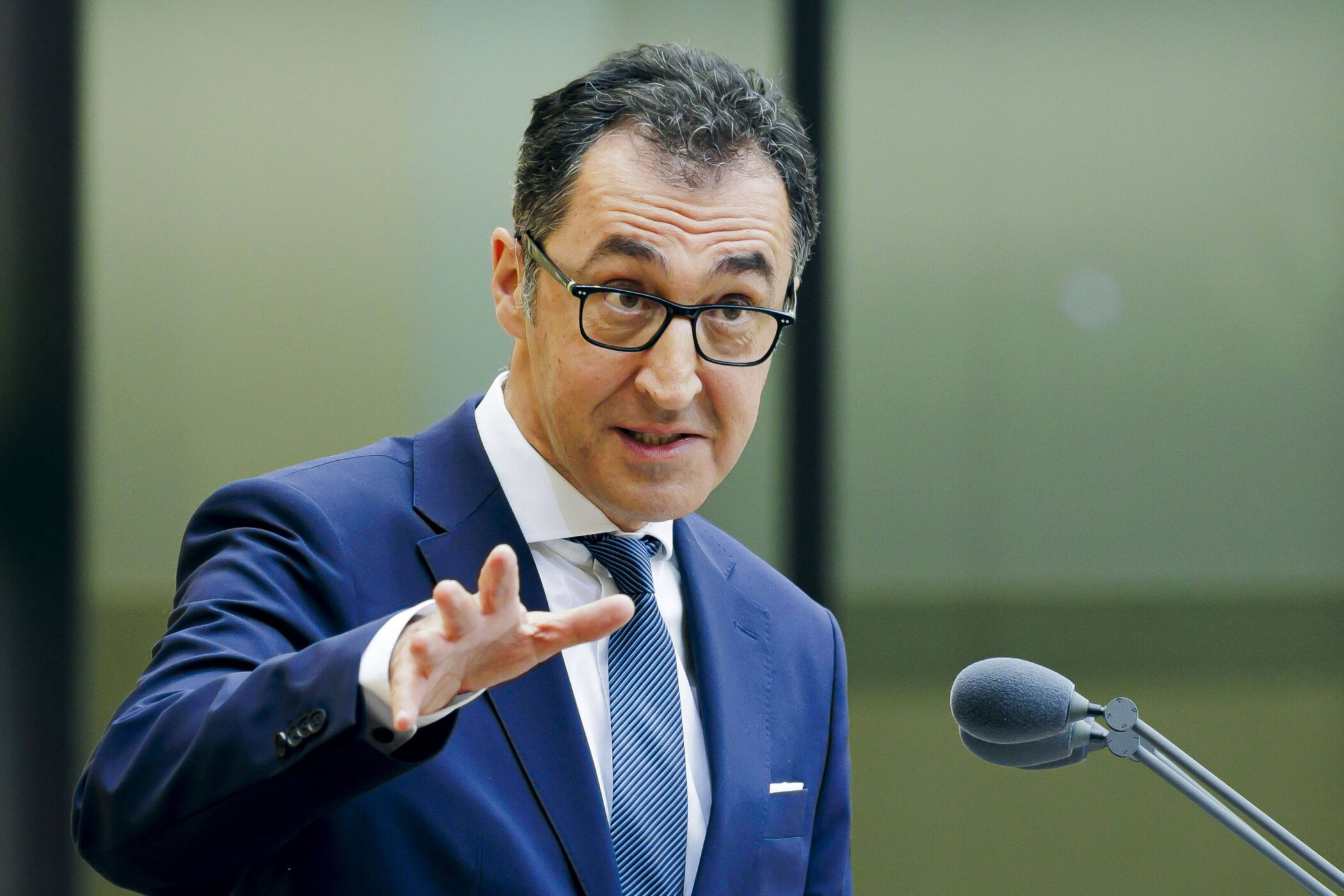 Mann mit Brille, Anzug und Krawatte spricht in ein Mikrofon.