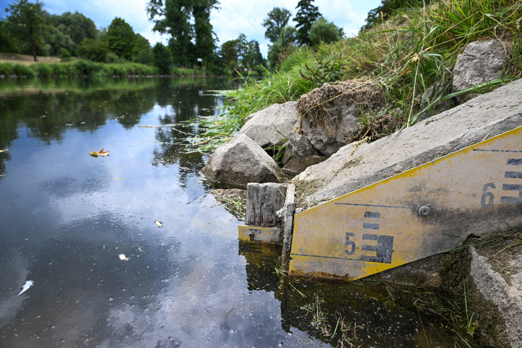 Wasserstandsanzeige mit gelben Markierungen neben einem Fluss.