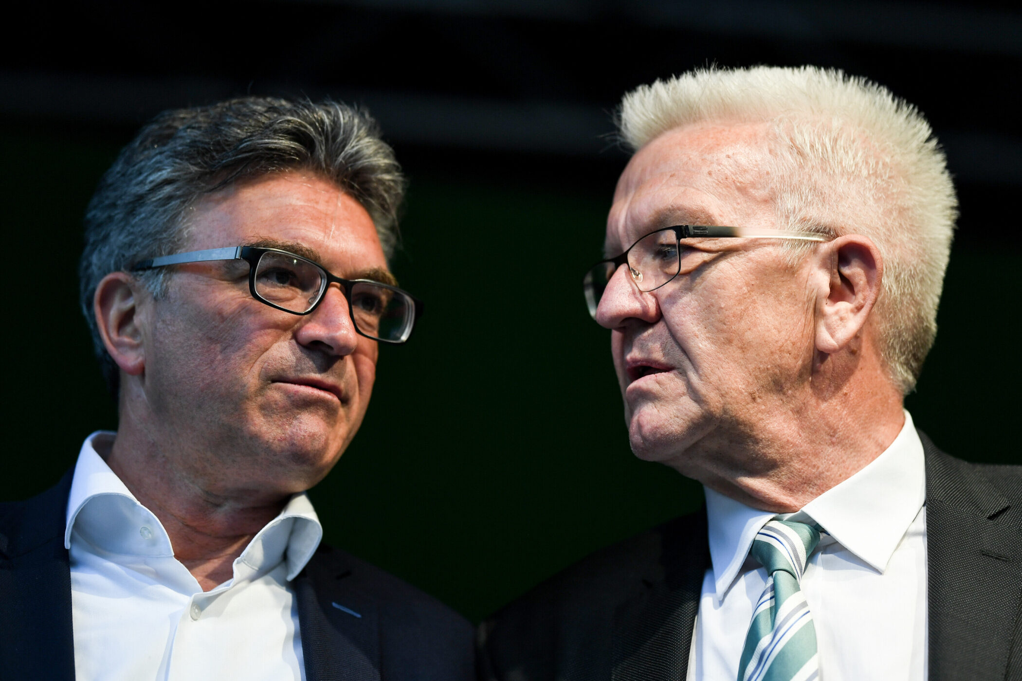 Zwei Männer im Anzug im Gespräch, beide tragen Brillen.