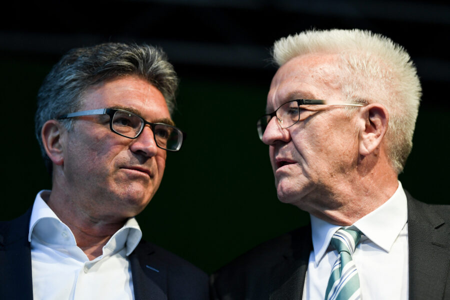 Zwei Männer im Anzug im Gespräch, beide tragen Brillen.