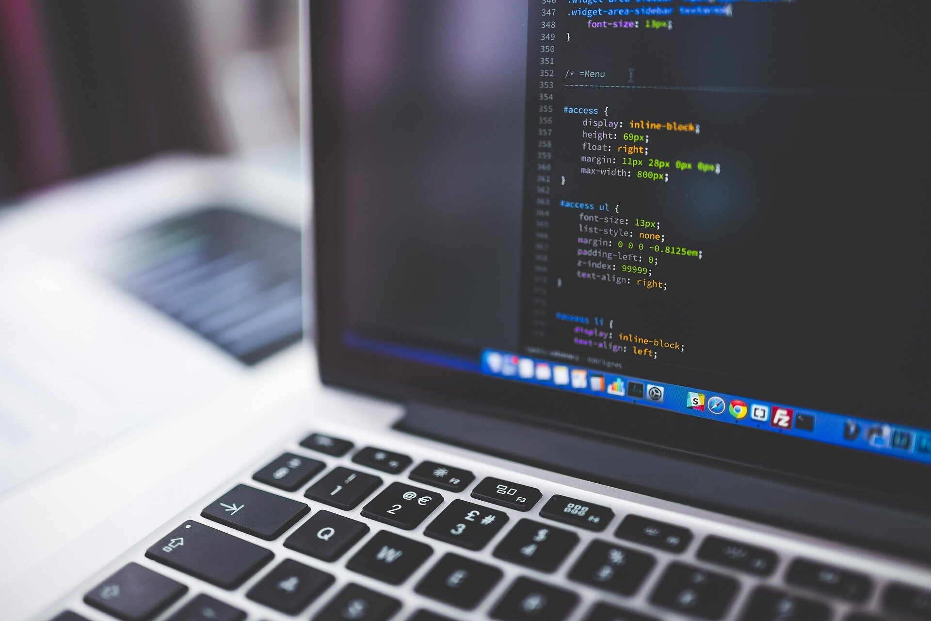 Laptop mit geöffneter Programmieroberfläche, Code auf Bildschirm. Tastatur sichtbar.