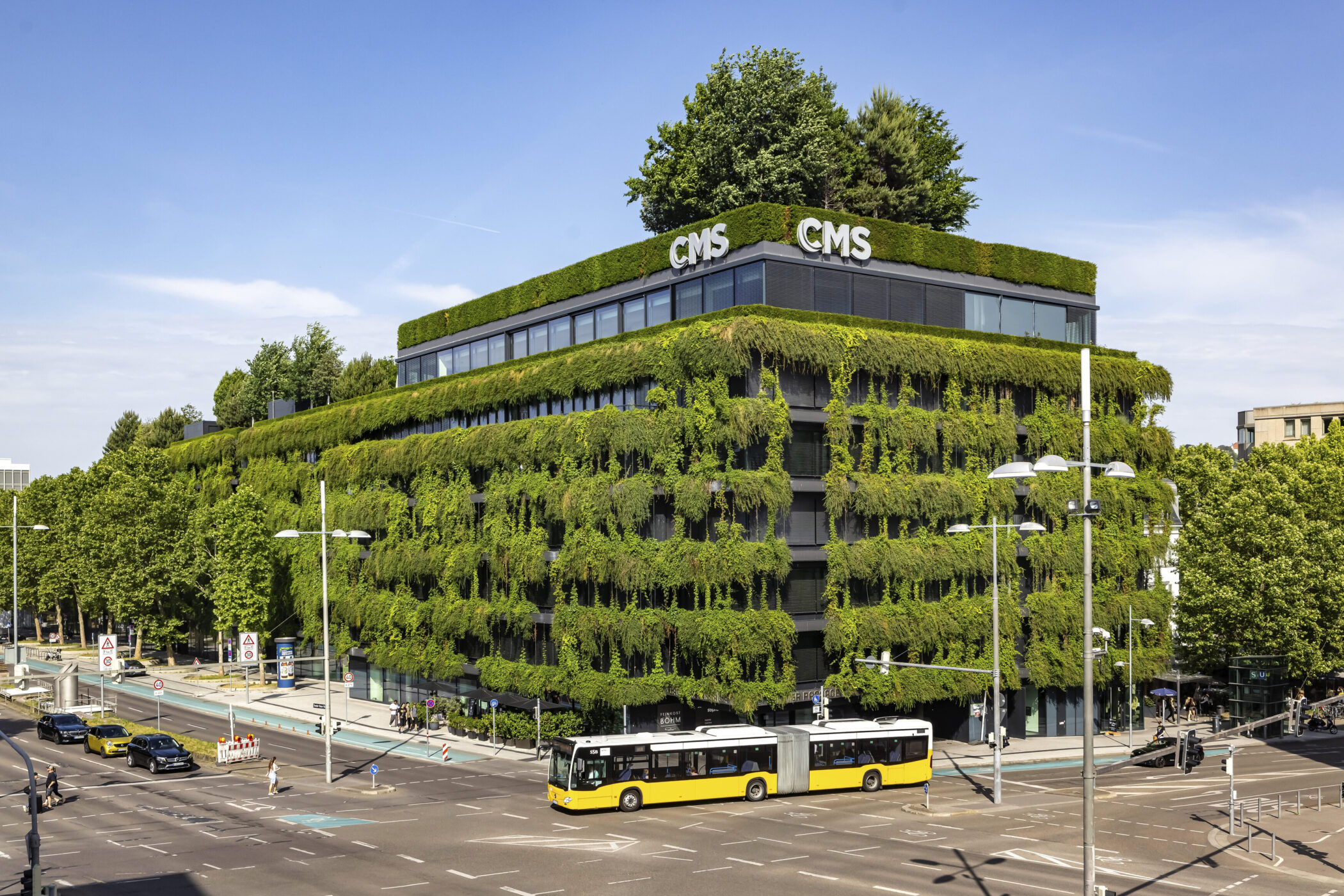 Rechteckiges Gebäude mit grüner Fassade, Bus und Autos auf der Straße.