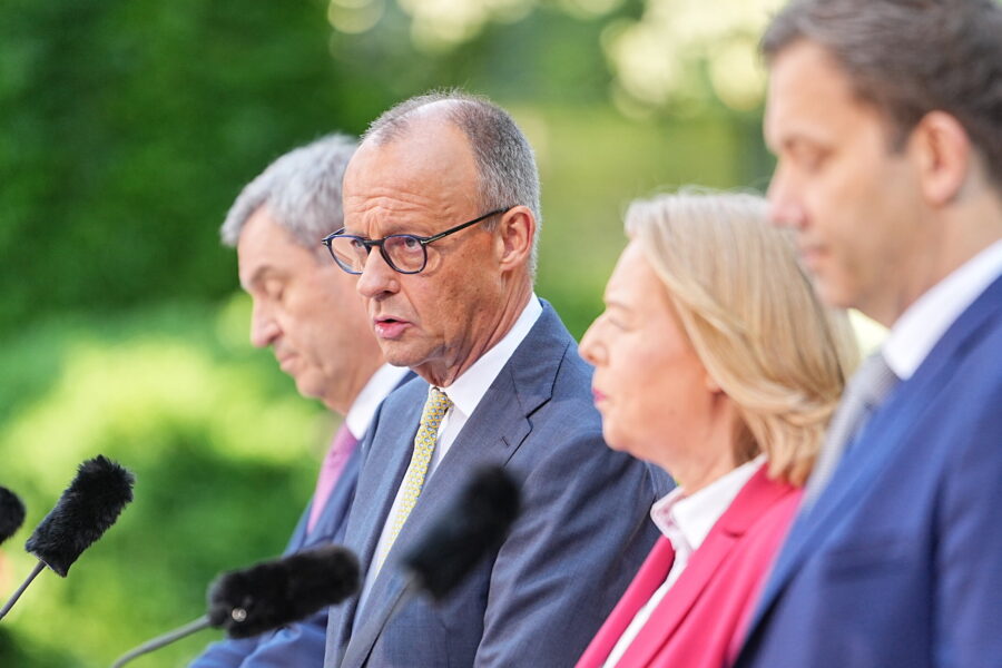 Vier Personen bei einer Pressekonferenz im Freien, Mikrofone vor ihnen.