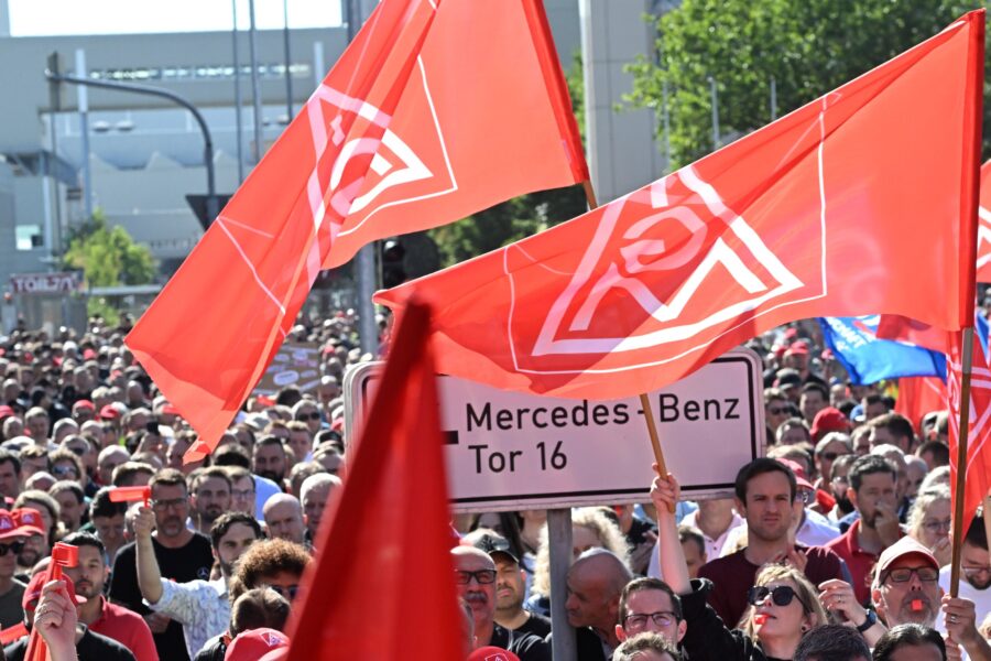 Menschenmenge mit roten Fahnen, Schild: "Mercedes-Benz Tor 16".