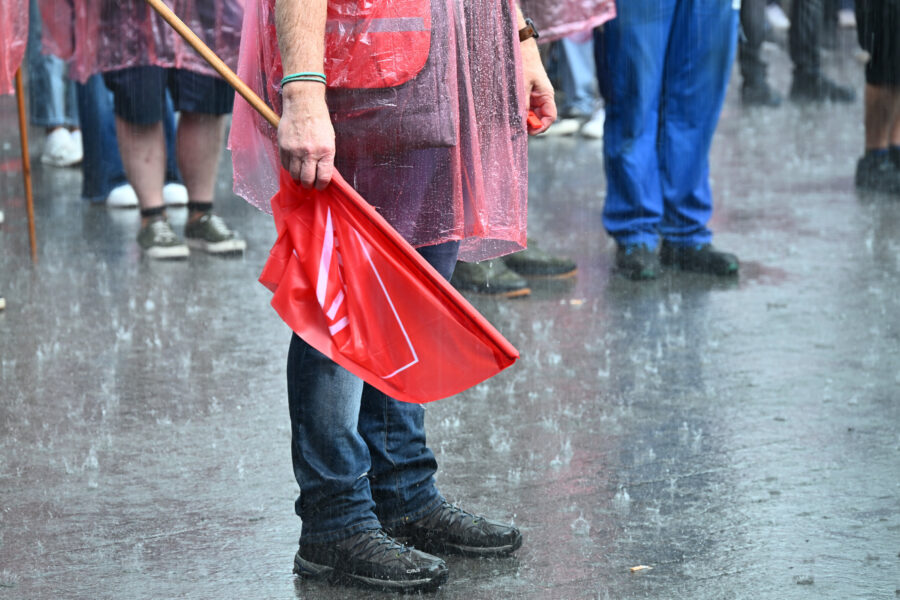 Person in Regenjacke mit roter Fahne im Regen, umgeben von weiteren Menschen.
