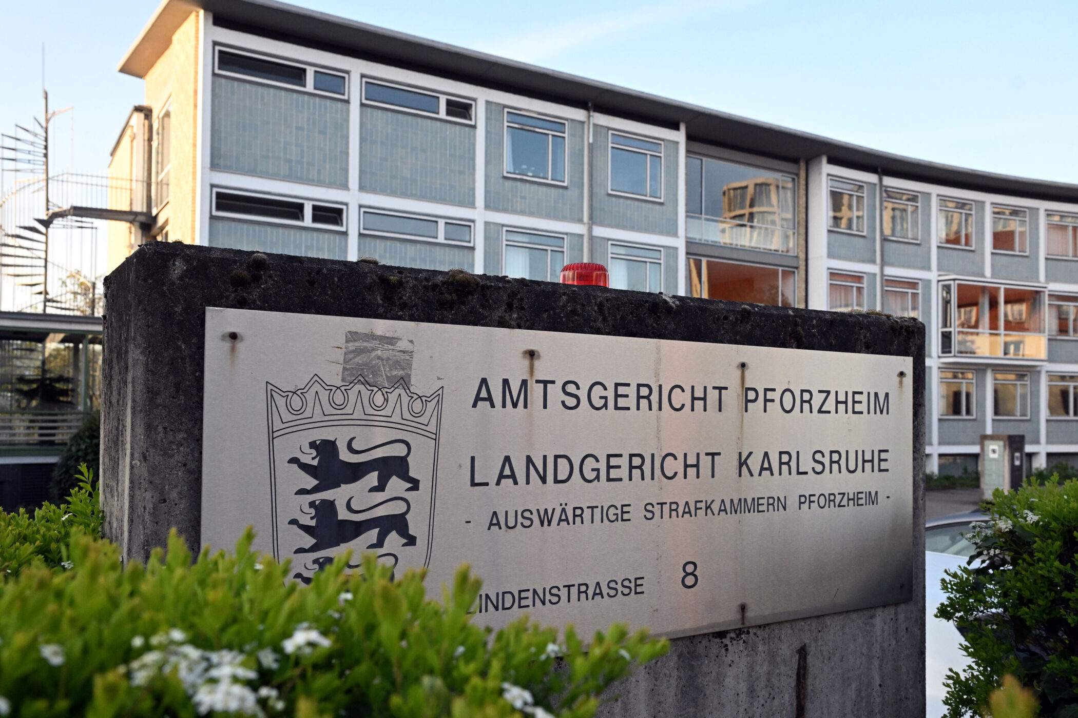 Schild mit "Amtsgericht Pforzheim", Gebäude dahinter, grüne Pflanzen im Vordergrund.