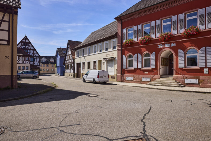 Straße mit Fachwerkhäusern, ein weißer Van, rotes Gebäude mit "Rathaus" Schriftzug.